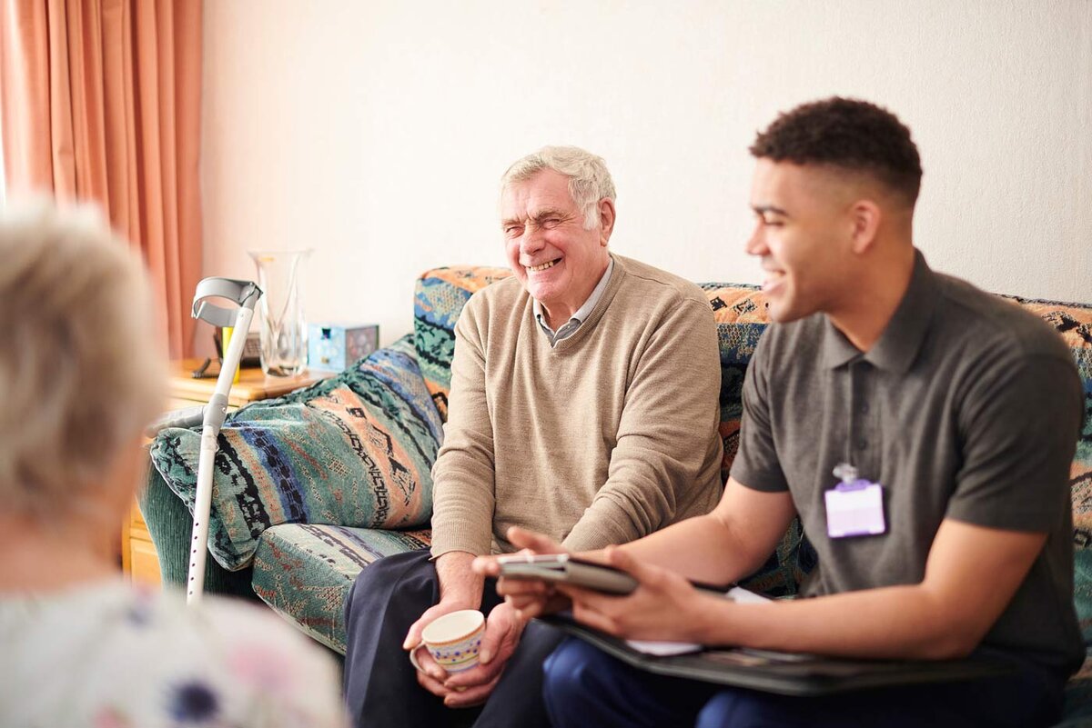 Elderly man and young aid sitting on a couch laughing