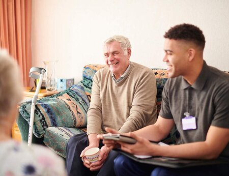 Elderly man and young aid sitting on a couch laughing