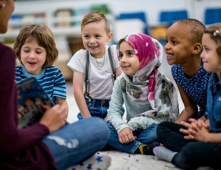 Children sitting in front of a teacher with a story book
